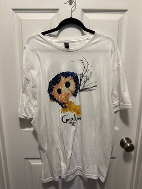White Coraline Graphic Tee with Blue & Yellow Design Regal Theatre 3D Anni